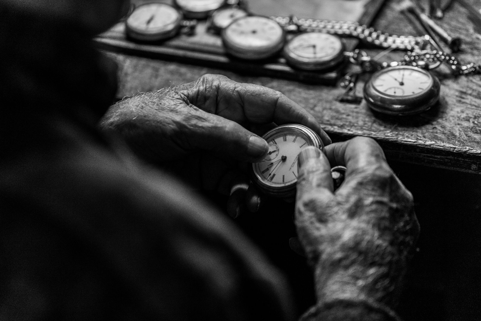 A craftsman's hands adjusting a pocket watch at a workbench